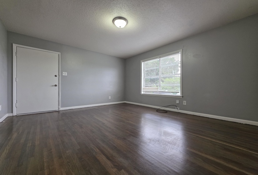 Spacious room featuring wood-finish flooring, a neutral color palette, a single window, a flush mount ceiling light, and base molding