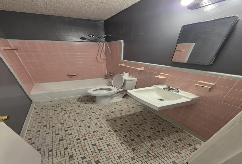 Bathroom featuring pink subway tile wainscoting, white bathtub with shower, white wall-mounted sink, and mosaic floor tile