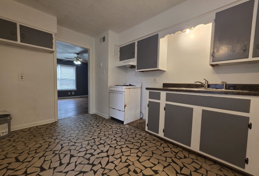 Kitchen featuring patterned floor tiles, white cabinetry with gray doors, dark speckled countertops, and a built-in sink with a gooseneck faucet