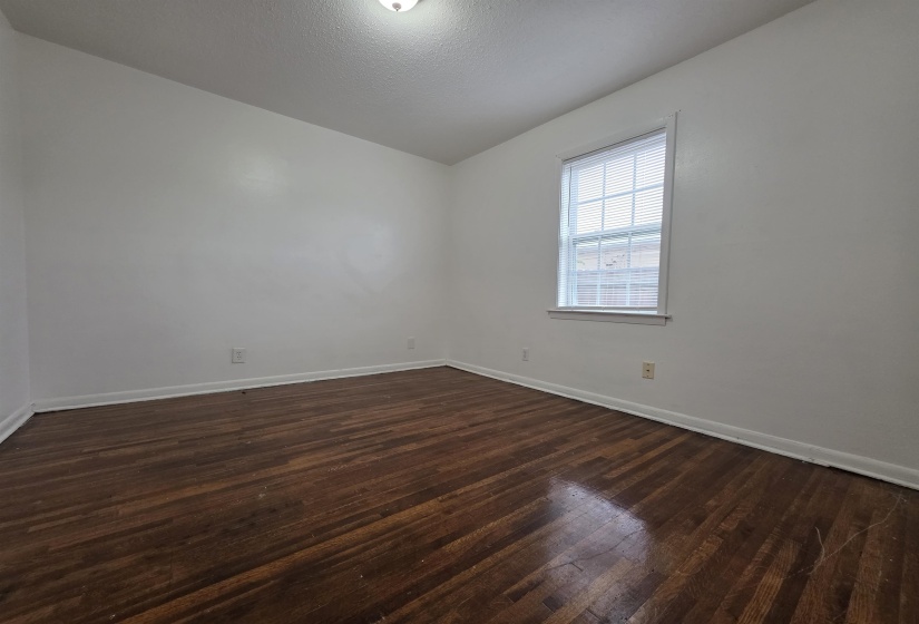 Room featuring wood-finish flooring, white painted walls, a single window with blinds, and white baseboards