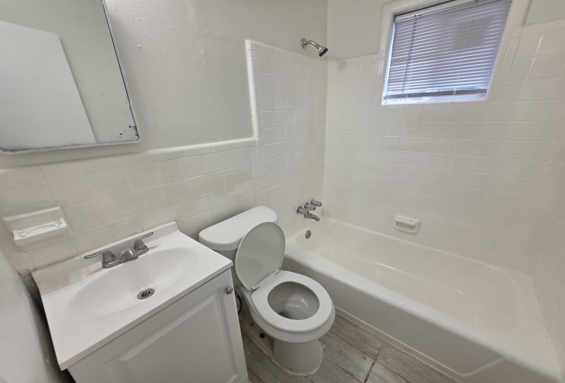 Bathroom featuring a bathtub with shower head, white tiled walls, a white vanity with sink, and a window with blinds