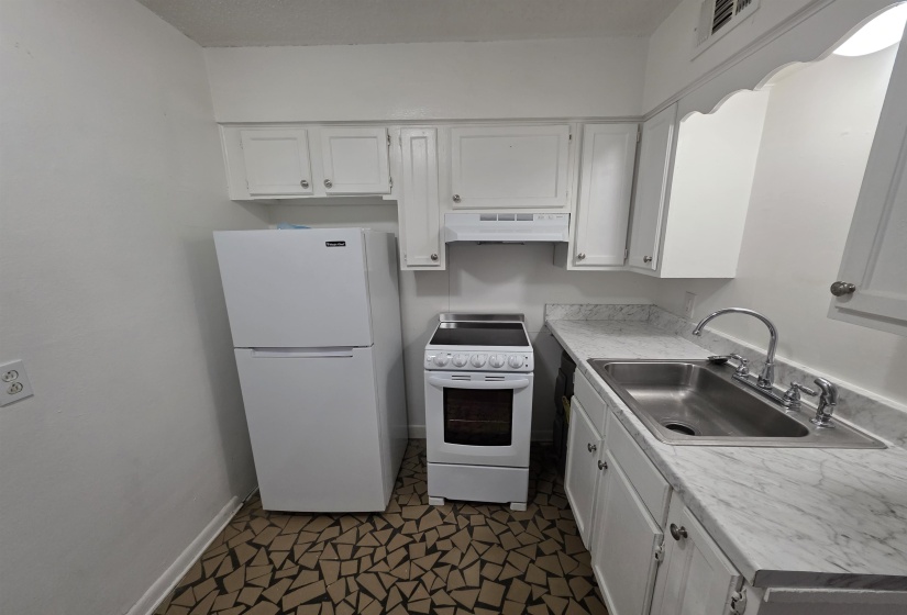 Kitchen featuring white cabinetry, white appliances, a stainless steel sink, and patterned floor tiling