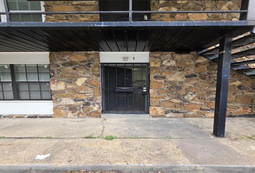 Stone facade building featuring a black metal security door and an overhead balcony with black metal railing