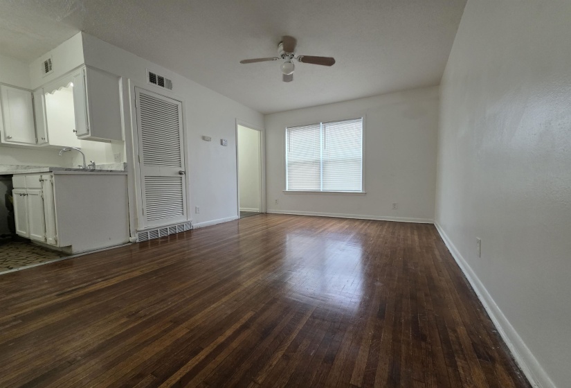 Spacious living area featuring rich wood-finish flooring, a white ceiling fan, and ample natural light from a double window