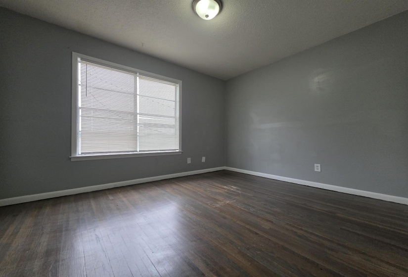 Spacious room featuring wood-finish flooring, a large window with blinds, and neutral gray wall tones