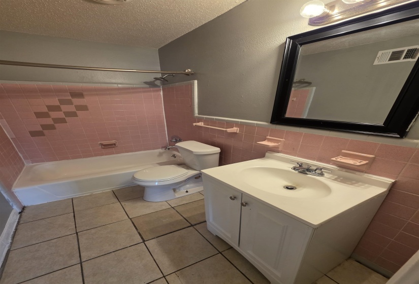 Bathroom featuring a white vanity with integrated sink, coordinating white commode, and a white bathtub with a shower
