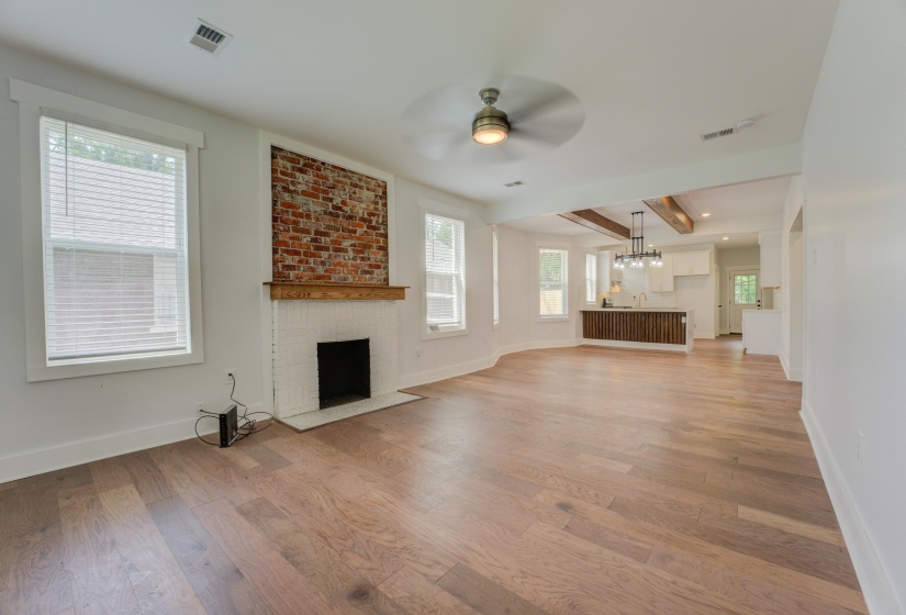 Spacious living area featuring wood-finish flooring, a brick accent wall with a white-tiled fireplace, and a ceiling fan