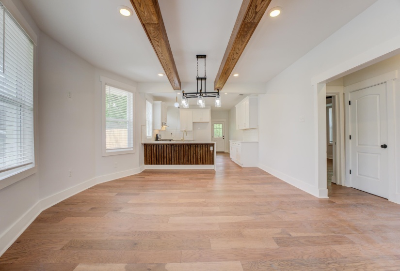 Spacious room with wood-finish flooring, exposed ceiling beams, recessed lighting, and a modern chandelier