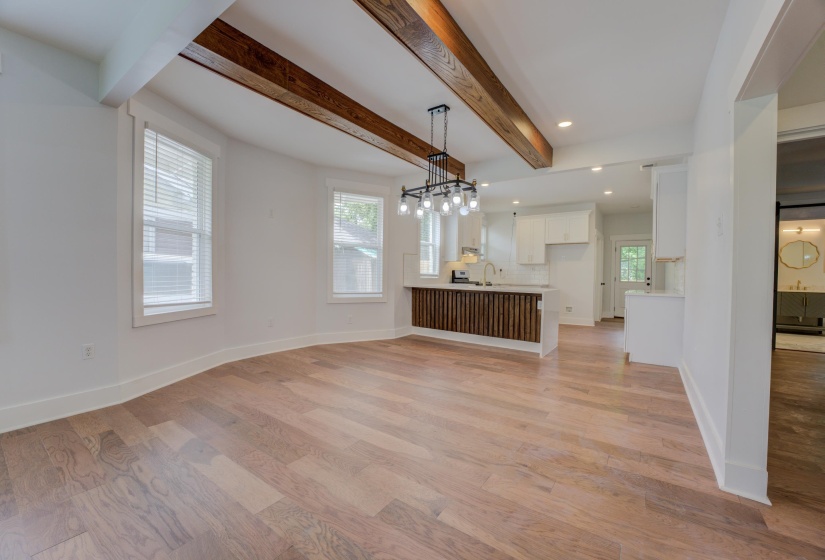 Expansive interior featuring wood-finish flooring, exposed ceiling beams, a contemporary chandelier, white walls, and bright windows