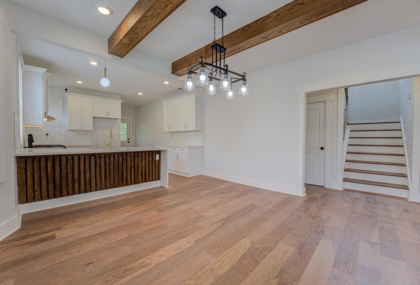 Open-concept living space featuring wood-finish flooring, exposed ceiling beams, a contemporary chandelier, and a kitchen island with a textured wood-panel front
