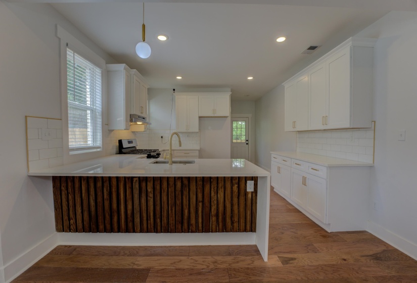Kitchen featuring a large island with a unique wood-slat base, white cabinetry, a gold-finish faucet, and a subway tile backsplash