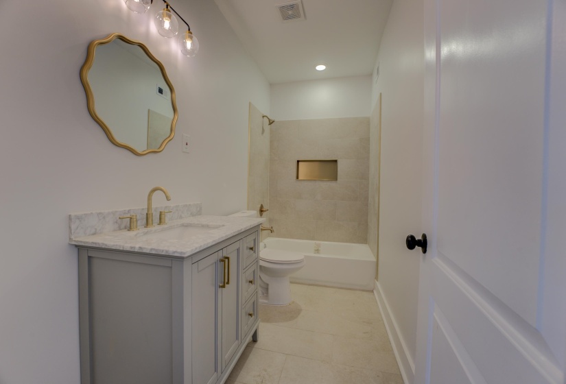 Modern bathroom featuring a gray vanity with a stone countertop, a gold-framed mirror, and a gold-finish faucet