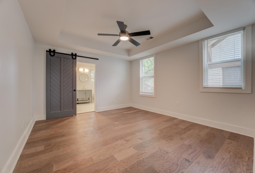 Spacious room featuring wood-finish flooring, a tray ceiling, and a ceiling fan with integrated lighting