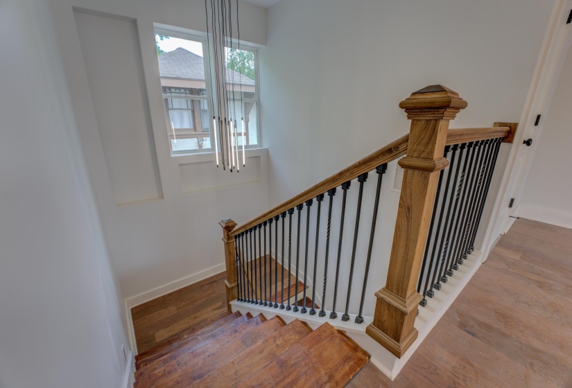 Hardwood staircase with wrought iron balusters and a wood-finish handrail, complemented by a contemporary linear chandelier