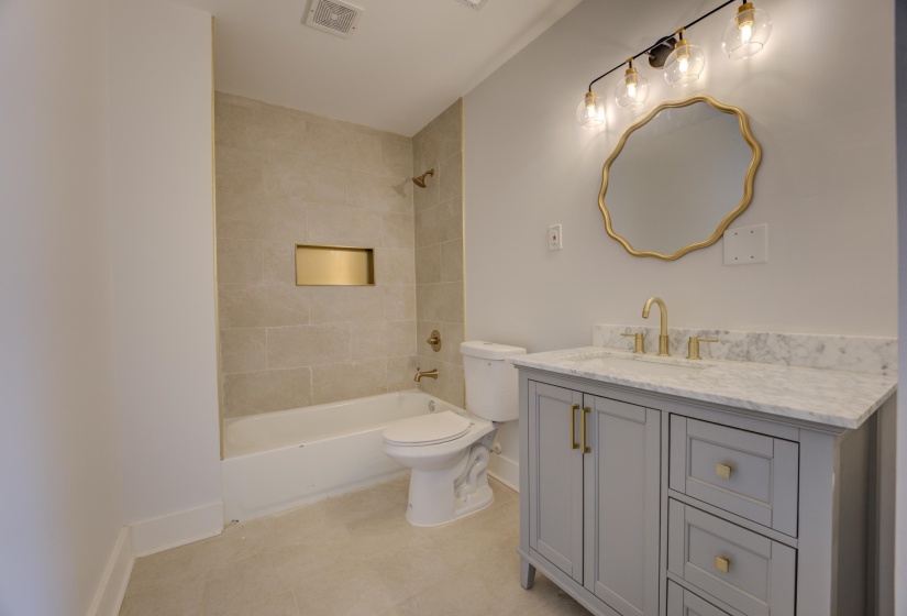 Bathroom featuring a light gray vanity with a stone countertop, a white porcelain tub with tiled surround, and gold-finish fixtures