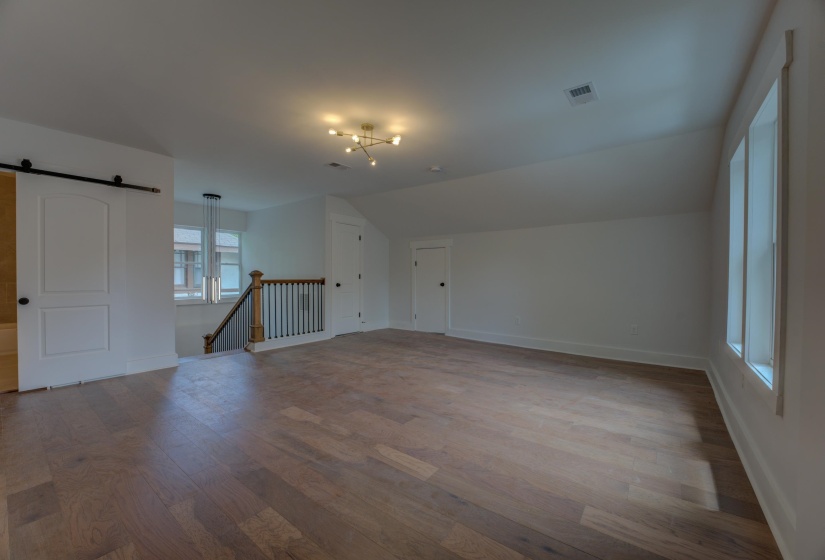 Spacious upper-level room featuring wood-finish flooring, a contemporary ceiling light fixture, and multiple windows providing natural light
