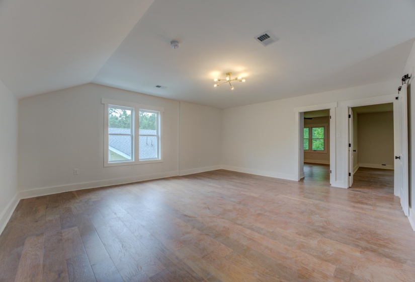 Spacious room featuring wood-finish flooring, white walls, and a contemporary ceiling light fixture