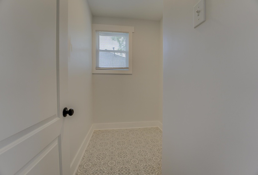 Compact interior space featuring patterned floor tile, white baseboards, a single window with blinds, and a white interior door with a black knob