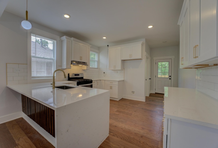 Kitchen featuring a central island with a waterfall-edge countertop and fluted wood-finish paneling, white shaker cabinetry with brass hardware, a stainless steel range and hood, white subway tile backsplash, and wood-finish flooring