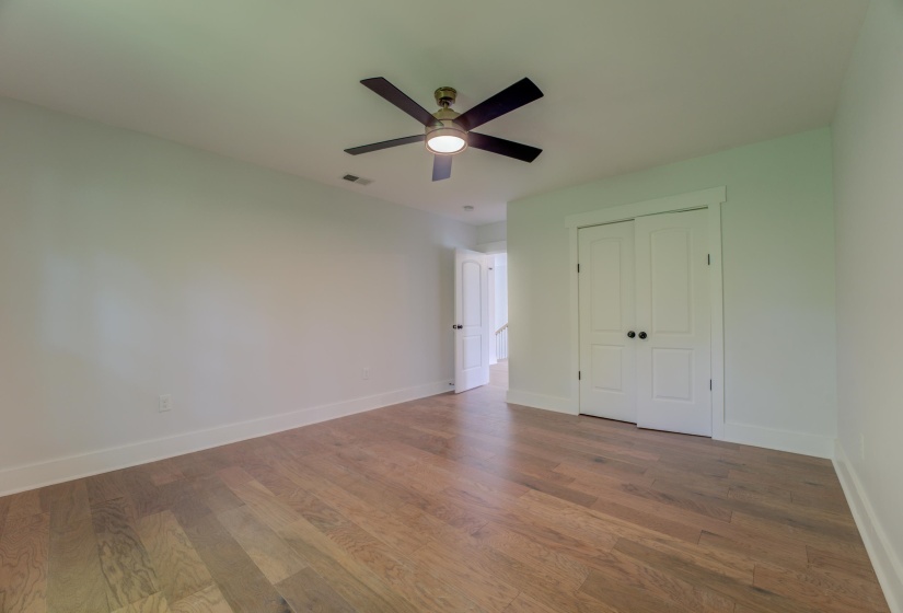 Spacious room featuring wood-finish flooring, a contemporary ceiling fan with integrated lighting, and white walls