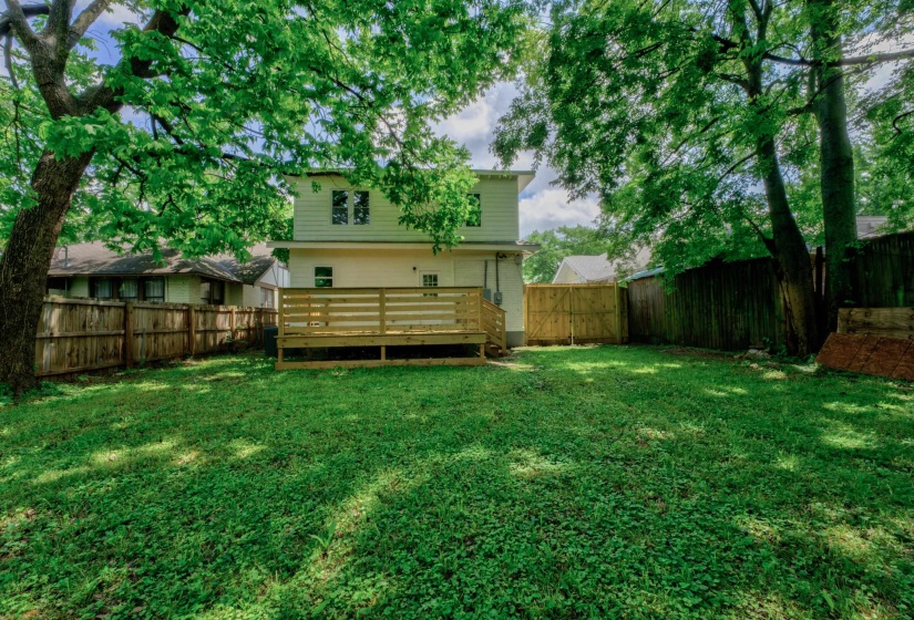 Expansive green lawn featuring a wooden deck, mature trees, and a privacy fence