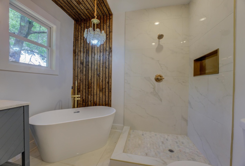 Freestanding soaking tub with a floor-mounted gold-finish faucet, complemented by a wood-paneled accent wall and an overhead chandelier