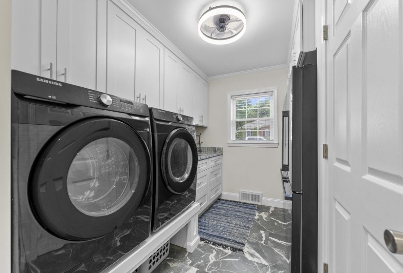 Well-appointed laundry room featuring abundant cabinetry, generous counter space, and a window that fills the room with natural light.