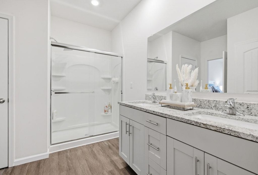 Primary bathroom featuring a double vanity with stone-finish countertops, dual undermount sinks, and light wood-finish flooring