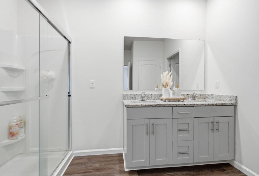 Dual sink vanity with stone countertop, mounted mirror, and wood-finish flooring