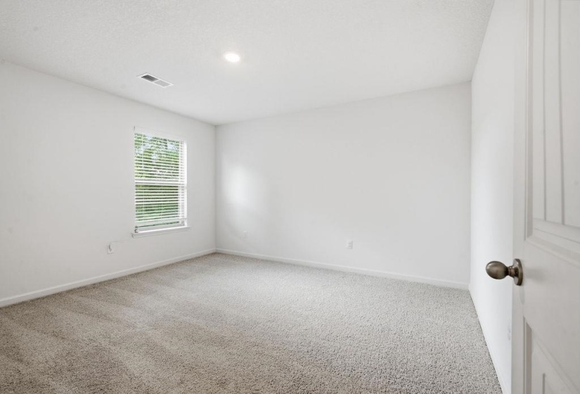 Neutral-toned carpeting extends throughout this room, featuring white painted walls and a single window with horizontal blinds