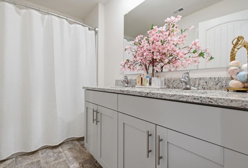 Double vanity with granite countertop and integrated sinks, modern gray cabinetry with brushed nickel hardware, and tiled flooring