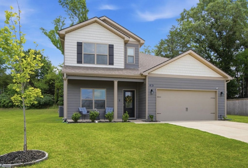 Two-story residence featuring a two-tone facade with horizontal siding and shingle accents, covered front porch, and an attached garage with a concrete driveway
