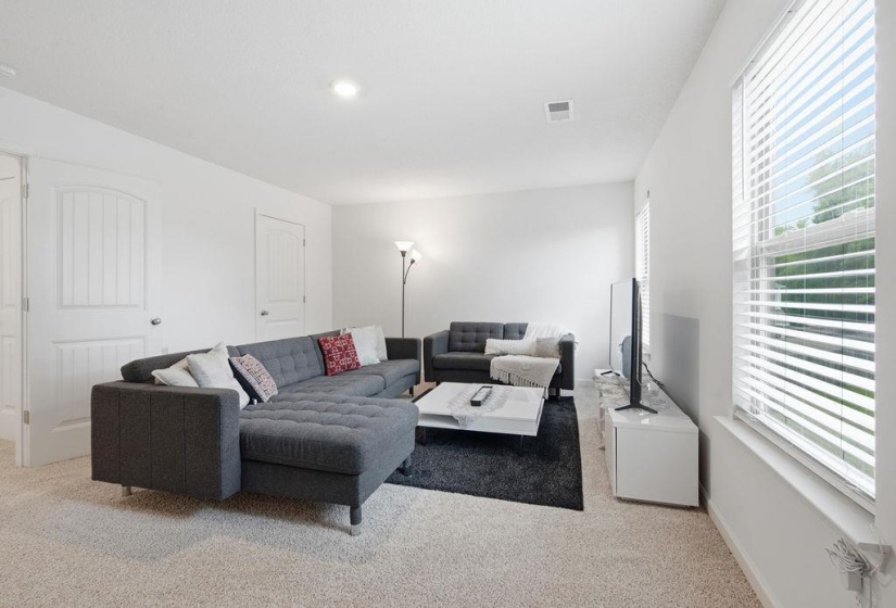 Bright living space featuring plush carpeting, dual windows with blinds, recessed lighting, and paneled interior doors