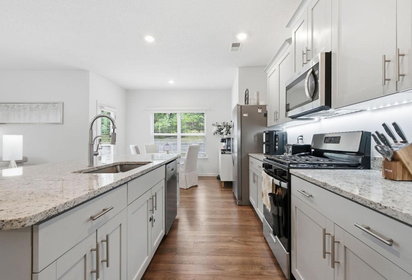 Open-concept kitchen featuring light-toned cabinetry, stainless steel appliances, a kitchen island with an undermount sink, and wood-finish flooring