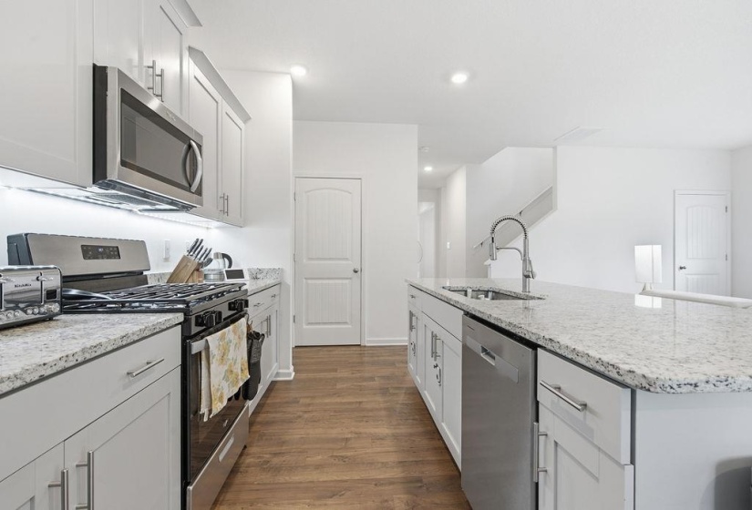Modern kitchen featuring wood-finish flooring, white cabinetry, granite countertops, stainless steel appliances, and an island with an integrated sink