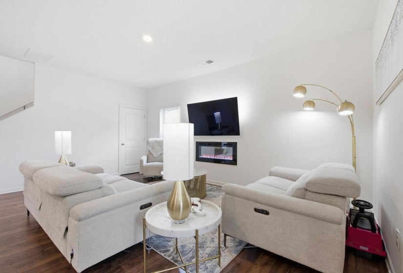 Living area featuring a wall-mounted television above a recessed electric fireplace, wood-finish flooring, and white walls