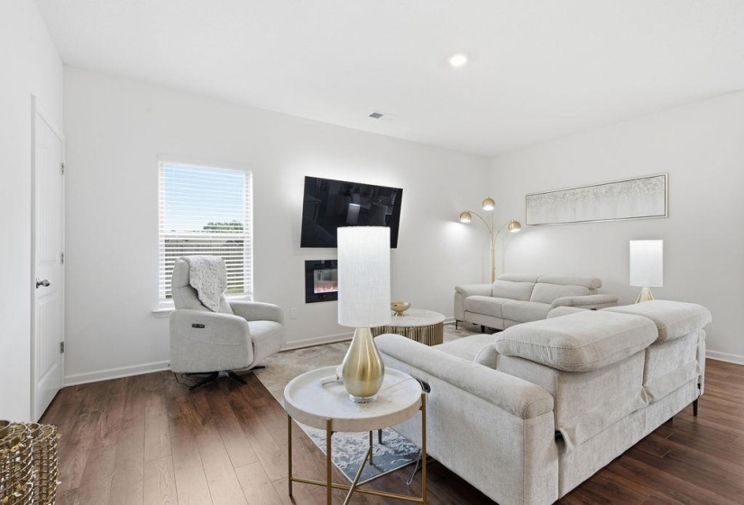 Spacious living area featuring wood-finish flooring, an electric fireplace, and a large window with blinds