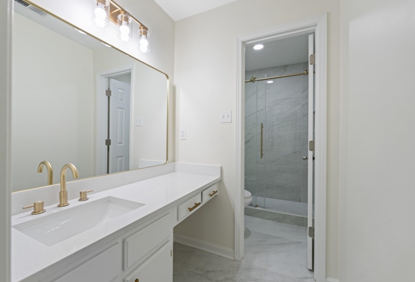 Beautifully updated primary bath featuring a granite vanity with makeup area, designer lighting, modern fixtures, tile flooring, and a clean, sophisticated design.