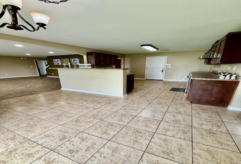 Spacious kitchen featuring large format tile flooring, dark wood-finish cabinetry, a stone-look countertop, and a built-in range hood