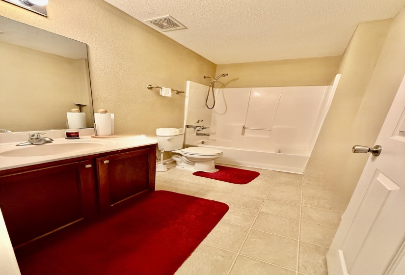 Bathroom featuring a white bathtub and shower combination, a vanity with a dark wood-finish cabinet and integrated sink, a wall-mounted mirror, and neutral-toned floor tiling