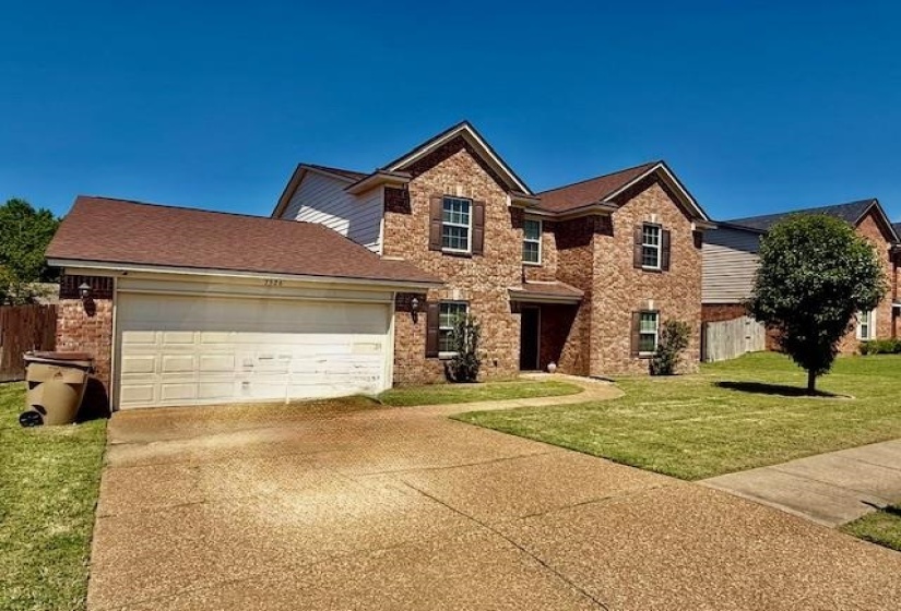 Brick exterior residence featuring a two-car garage, mature landscaping, and a concrete driveway