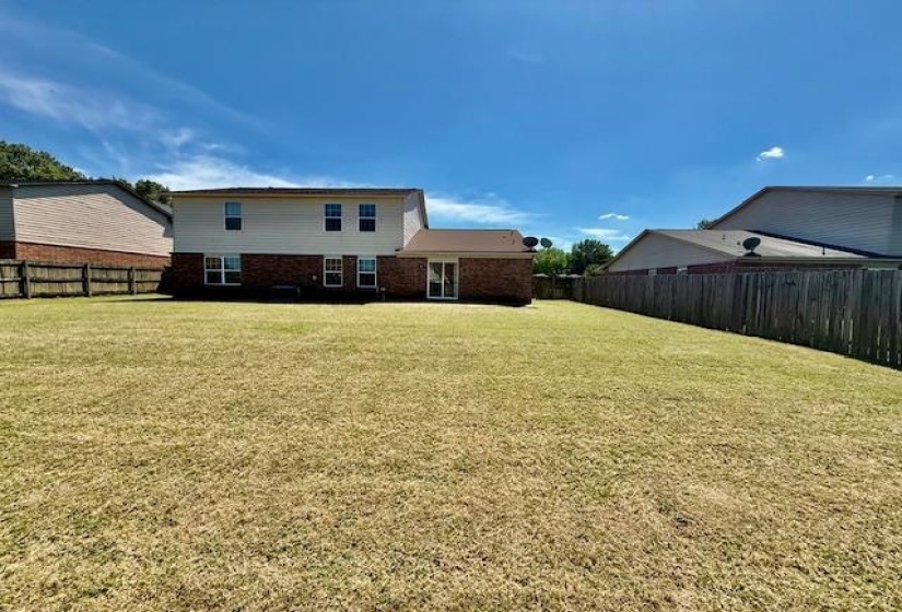 Expansive backyard featuring a large green space, privacy fencing, and a brick and siding exterior with multiple windows