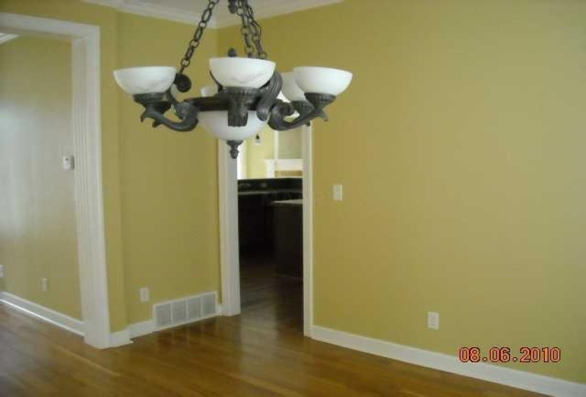 Dining area featuring a five-light chandelier with frosted glass shades and dark-toned metalwork, wood-finish flooring, and white baseboards