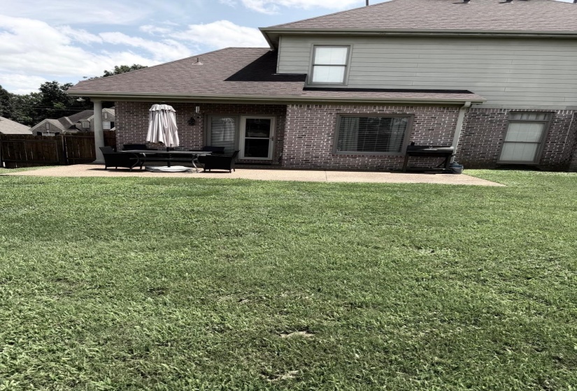 Expansive backyard featuring a large concrete patio, brick exterior, and partial privacy fencing