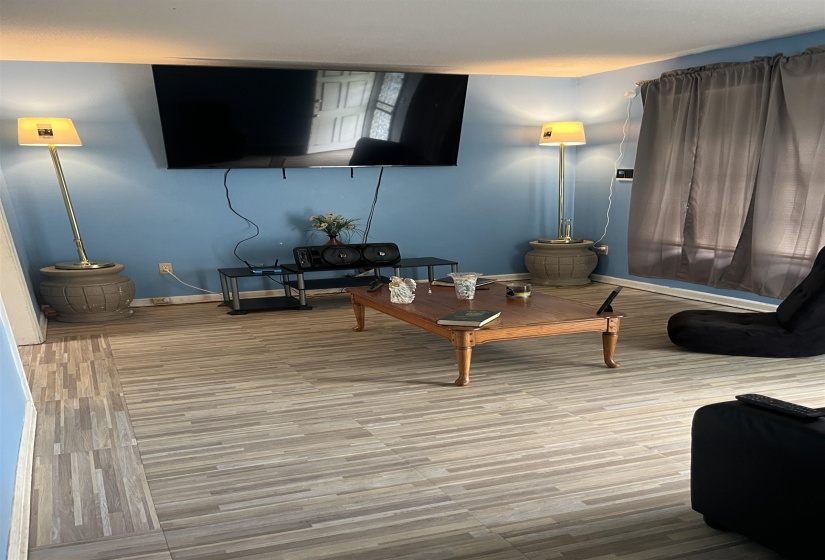 Living area featuring plank-style flooring, a wall-mounted television, and light blue wall paint