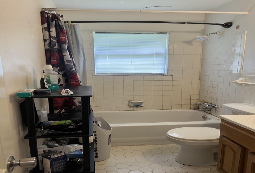 Bathroom featuring a white bathtub, white tiled walls, and a window with blinds
