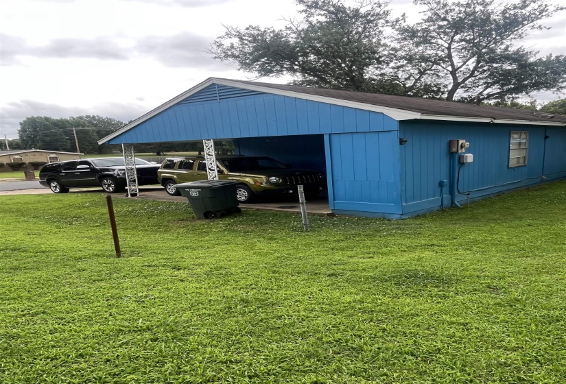 Blue-sided structure with a covered carport, featuring a gabled roof and a side window
