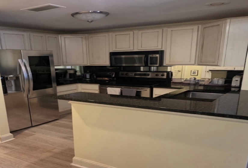 Kitchen featuring light-toned cabinetry, stainless steel appliances, dark stone countertops, and wood-finish flooring