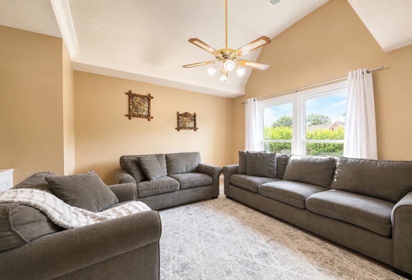Living area featuring a vaulted ceiling with crown molding, a ceiling fan with integrated lighting, and light-toned walls