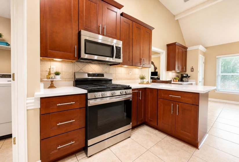 Kitchen featuring wood cabinetry, stainless steel appliances, white countertops, tile backsplash, and tile flooring